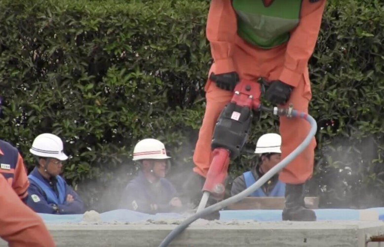 hombre con overol rojo usando y botas de trabajo usando un martillo demoledor